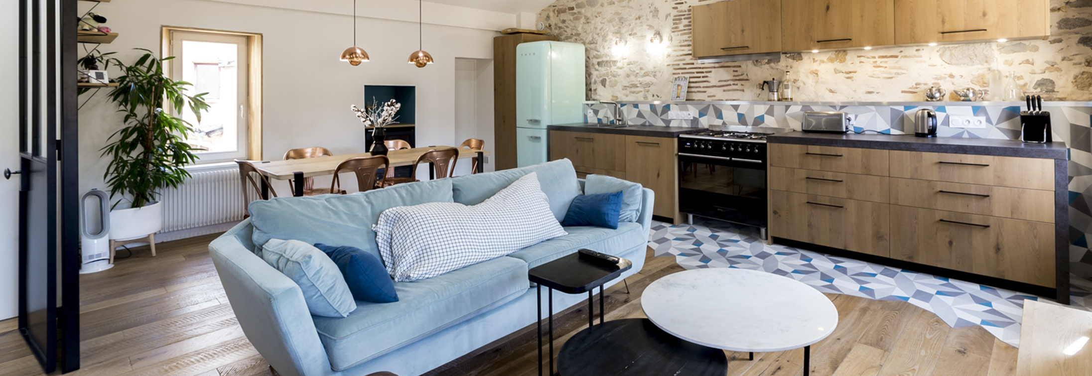 Publication presse dans le magazine Avenue 70. La réalisation de Skéa Designer, Bleu Affluent est mise à l'honneur. Sur la photo, le salon avec son canapé vert amande, puis la cuisine ouverte avec ses carreaux de ciments bleu au motif géométrique et le plan de travail en céramique, puis la table en bois Tip Toe et les chaises Cuivrées.
