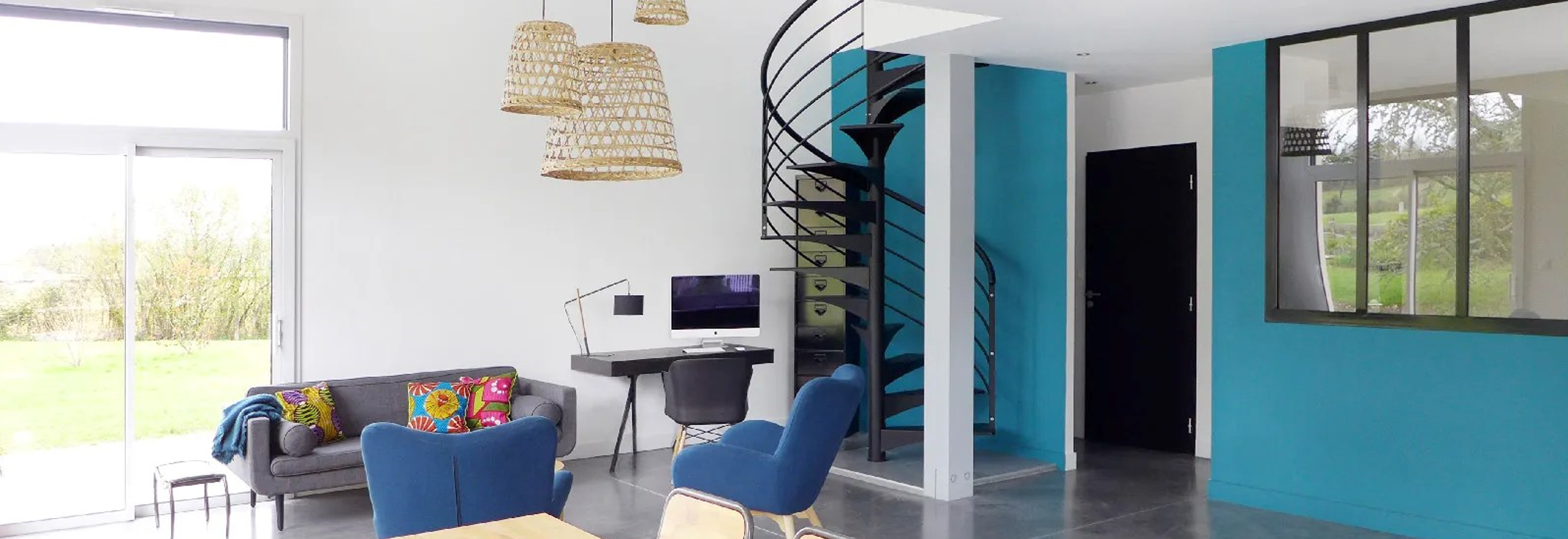 Publication dans le Journal de Québec. Les réalisations du studio d'architecture d'intérieur et de décoration Skéa Designer sont mises à l'honneur. Ici un salon avec un béton ciré gris au sol, un mur bleu canard et un escalier hélicoïdale noir.